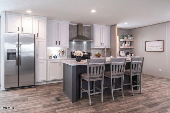 913 Henry Harr Rd, Blountville, TN 37617 - kitchen with stainless steel refrigerator with ice dispenser, wall chimney exhaust hood, light countertops, wood finished floors, and an island with sink