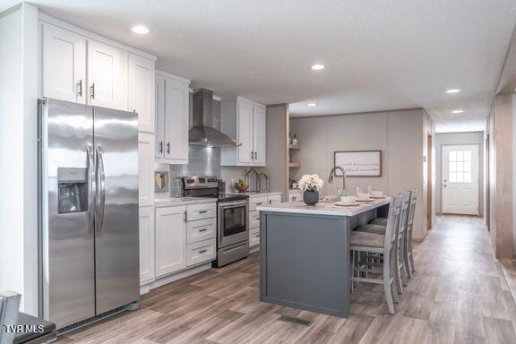 913 Henry Harr Rd, Blountville, TN 37617 - kitchen featuring appliances with stainless steel finishes, wall chimney range hood, light countertops, light wood-style flooring, and a center island with sink