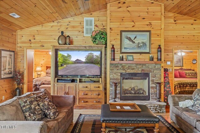 2213 Woodcock Trl, Sevierville, TN 37876 - living area with lofted ceiling, wooden walls, wood ceiling, a stone fireplace, and wood finished floors
