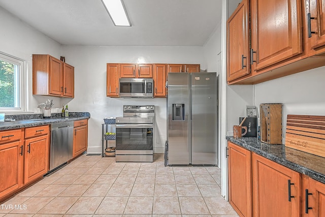 218 W Banner St, Lebanon, VA 24266 - kitchen featuring appliances with stainless steel finishes, brown cabinets, light tile patterned floors, dark stone counters, and baseboards