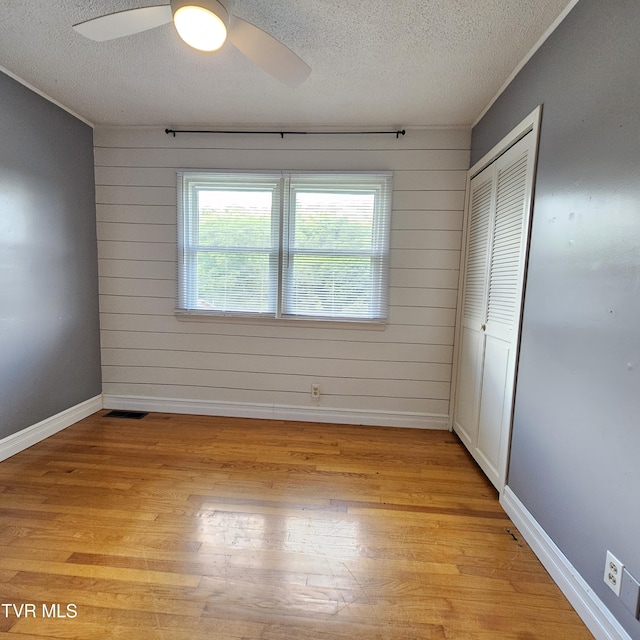 515 Chuckey Pike, Chuckey, TN 37641 - unfurnished bedroom featuring a textured ceiling, light wood finished floors, a closet, wood walls, and ceiling fan