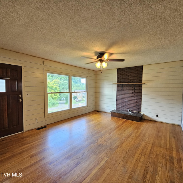 515 Chuckey Pike, Chuckey, TN 37641 - unfurnished living room featuring wood finished floors, a textured ceiling, ceiling fan, wood walls, and a brick fireplace