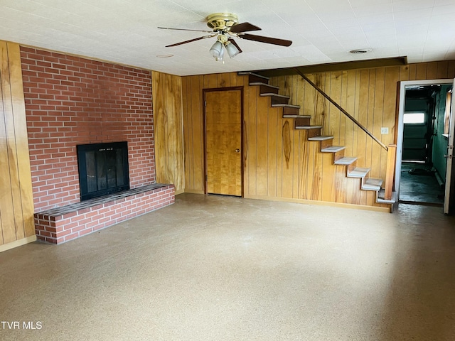 201 Brown St, Appalachia, VA 24216 - unfurnished living room with baseboards, wooden walls, a ceiling fan, a brick fireplace, and stairway