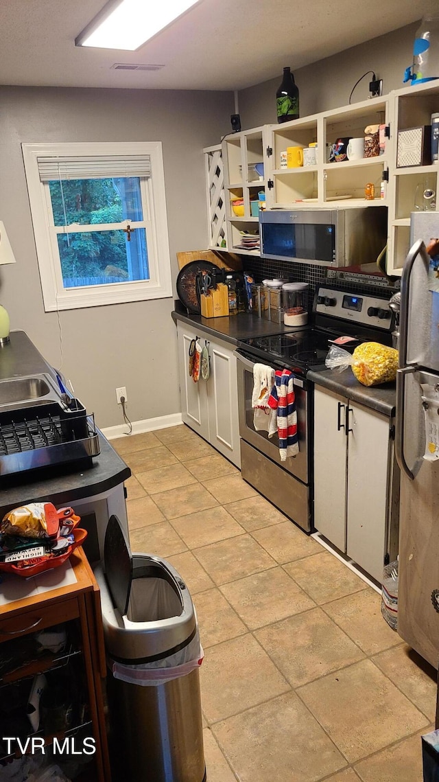 1315 Lowe St, Elizabethton, TN 37643 - kitchen featuring stainless steel appliances, dark countertops, light tile patterned floors, baseboards, and white cabinetry