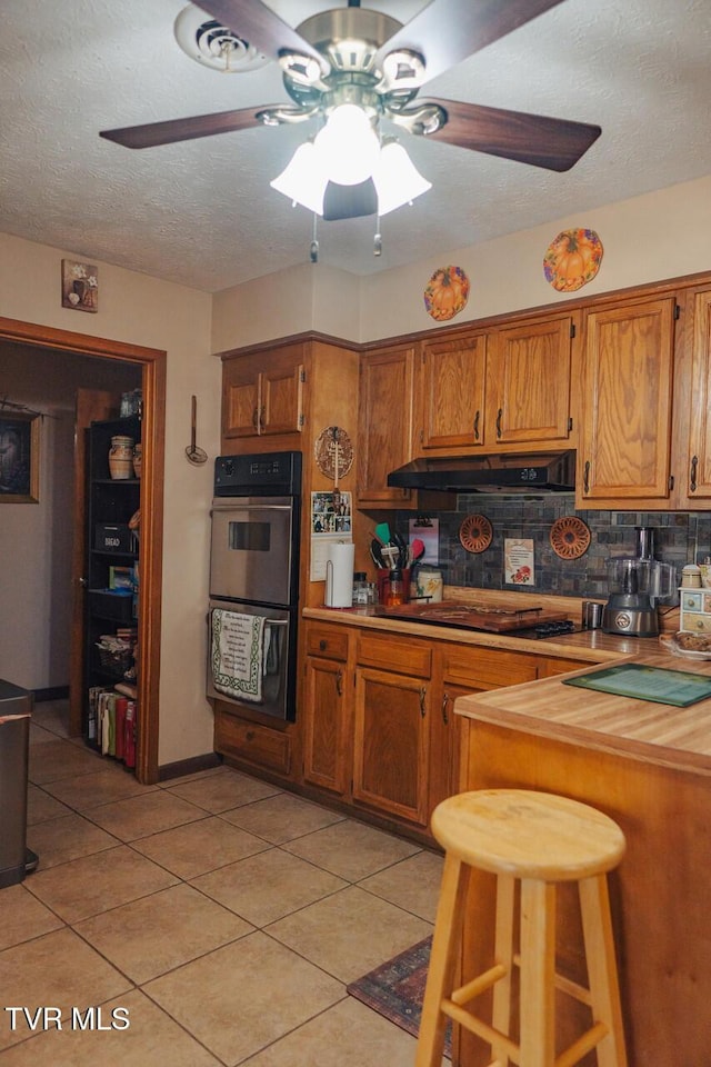 3521 James Phillips Way, Sevierville, TN 37876 - kitchen with stainless steel double oven, a ceiling fan, brown cabinets, under cabinet range hood, and light tile patterned floors