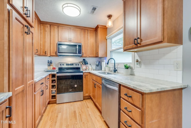 1933 Sand St, Kingsport, TN 37660 - kitchen with stainless steel appliances, light wood-style flooring, backsplash, light stone counters, and brown cabinetry
