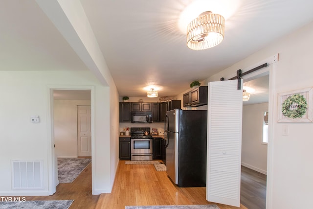 2637 Bay St, Bristol, TN 37620 - kitchen with appliances with stainless steel finishes, a barn door, light wood finished floors, dark brown cabinetry, and a chandelier