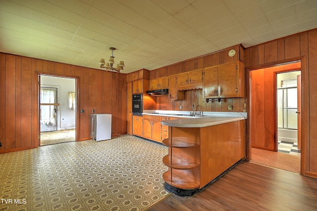 325 Cove Creek Rd, Roan Mountain, TN 37687 - kitchen with wood walls, black oven, brown cabinetry, a peninsula, and a chandelier