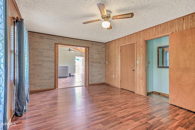 307 Tween Hills Rd, Bristol, TN 37620 - spare room featuring a ceiling fan, wood finished floors, wooden walls, brick wall, and a textured ceiling