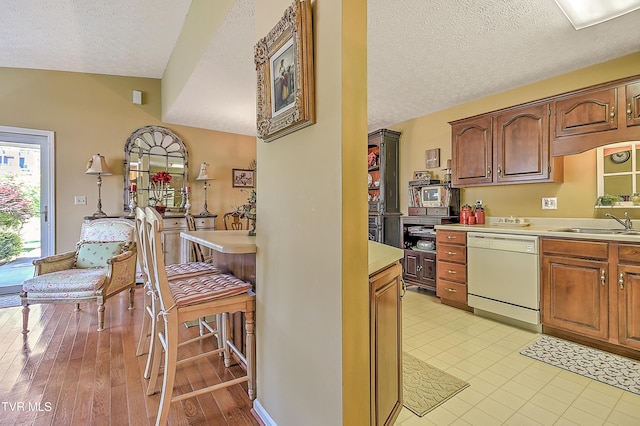 713 Teasel Dr Unit 0, Kingsport, TN 37660 - kitchen with white dishwasher, a textured ceiling, light countertops, a breakfast bar, and brown cabinets