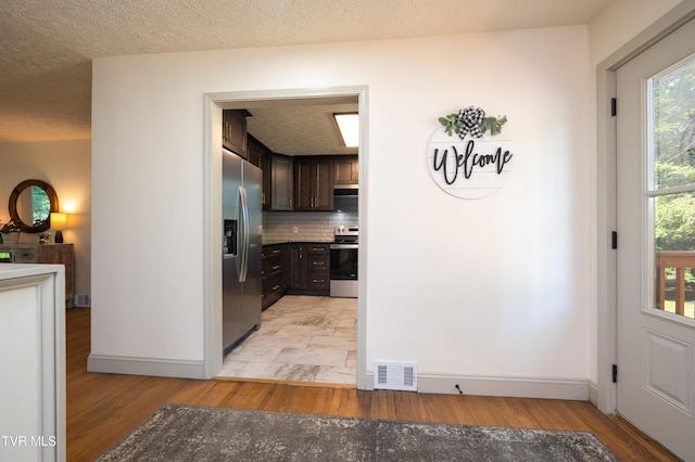 101 Ridgewood Dr, Bristol, TN 37620 - kitchen featuring appliances with stainless steel finishes, backsplash, dark brown cabinetry, light wood-style floors, and a textured ceiling