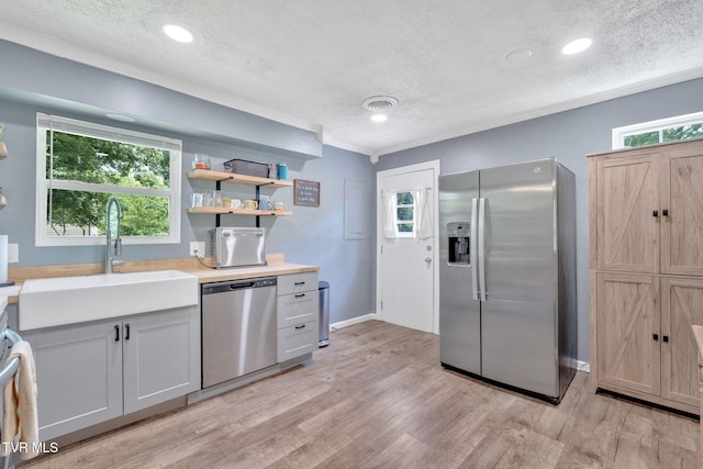 8202 Westland Dr, Knoxville, TN 37919 - kitchen featuring appliances with stainless steel finishes, a textured ceiling, light countertops, light wood-style floors, and ornamental molding