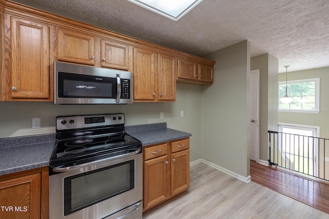 5630 Orebank Rd, Kingsport, TN 37664 - kitchen featuring appliances with stainless steel finishes, brown cabinetry, dark countertops, light wood-style flooring, and a textured ceiling