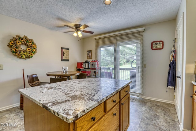223 Willowbend Ct, Kingsport, TN 37660 - kitchen featuring ceiling fan, brown cabinets, a kitchen island, a textured ceiling, and light stone counters