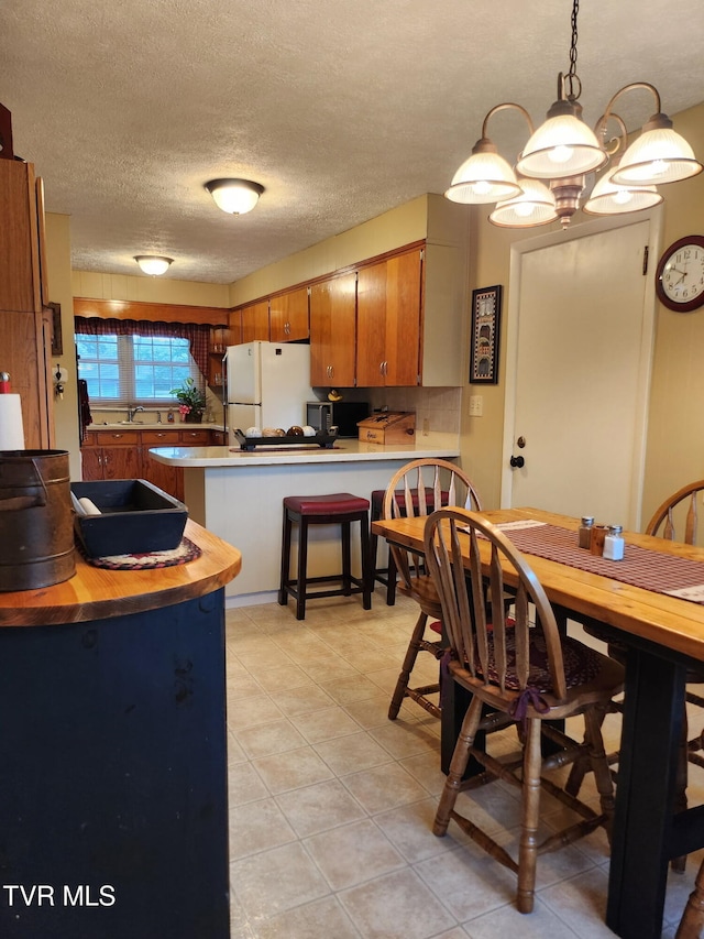 2020 Oakland St, Kingsport, TN 37660 - kitchen with freestanding refrigerator, a peninsula, light tile patterned flooring, brown cabinetry, and a textured ceiling