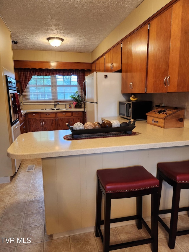 2020 Oakland St, Kingsport, TN 37660 - kitchen featuring appliances with stainless steel finishes, a peninsula, light countertops, brown cabinetry, and a textured ceiling