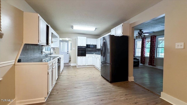 542 Sigman Hollow Rd, Bluff City, TN 37618 - kitchen with refrigerator with ice dispenser, black oven, a ceiling fan, light wood finished floors, and tasteful backsplash