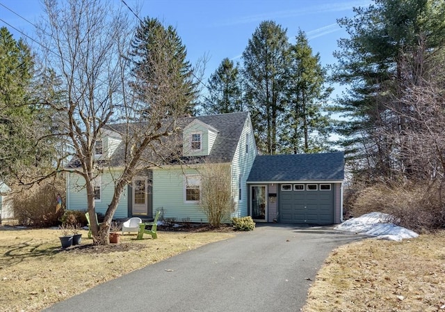 new england style home featuring driveway, a shingled roof, and a garage
