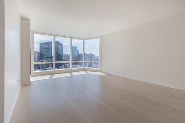 unfurnished room with expansive windows, a city view, baseboards, and wood finished floors