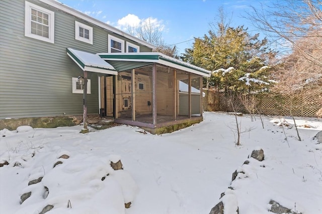 snow covered property with a garage, fence, and a sunroom