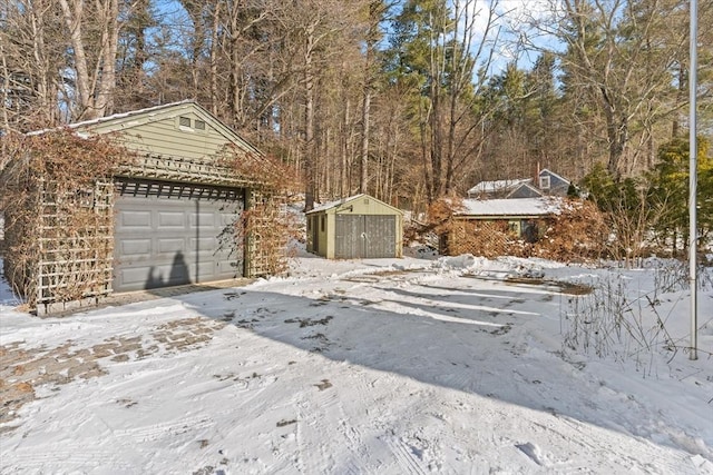 snowy yard with an attached garage, a storage shed, and an outdoor structure