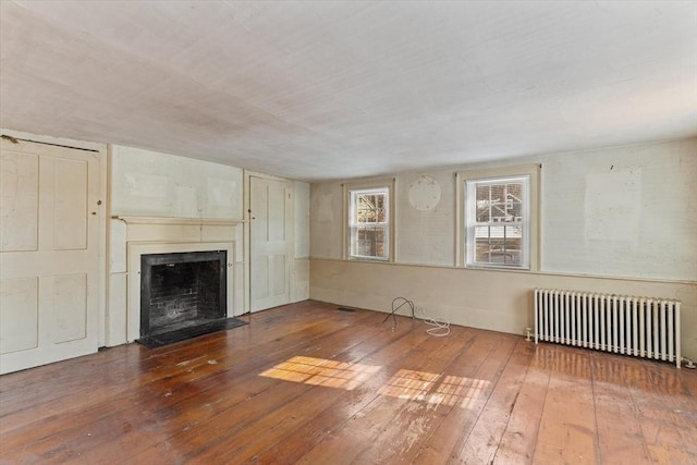 unfurnished living room with a fireplace with flush hearth, hardwood / wood-style floors, and radiator heating unit