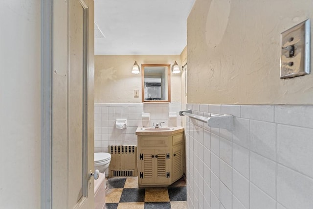 bathroom with a wainscoted wall, tile walls, toilet, radiator heating unit, and tile patterned floors