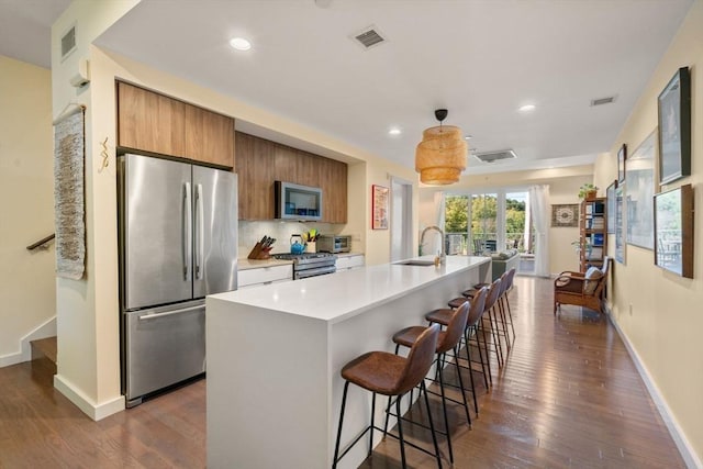 kitchen featuring appliances with stainless steel finishes, a kitchen breakfast bar, a kitchen island with sink, dark wood-type flooring, and sink