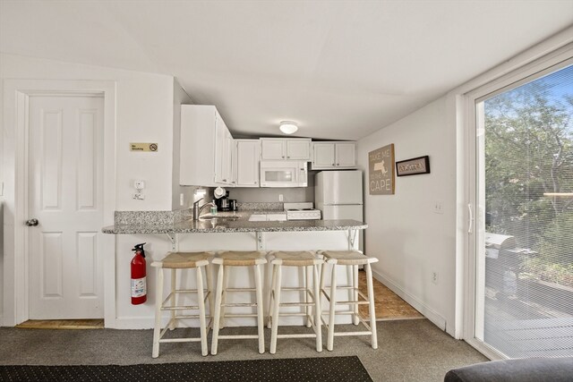 kitchen featuring lofted ceiling, kitchen peninsula, white appliances, white cabinetry, and a breakfast bar