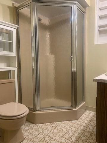 bathroom featuring tile patterned floors, toilet, vanity, and a shower stall