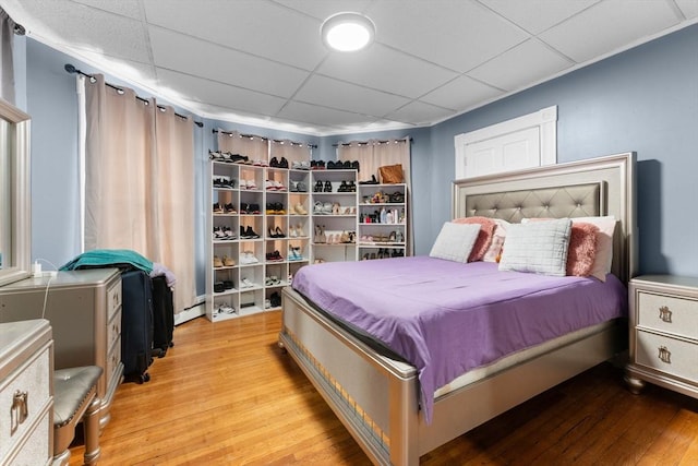 bedroom featuring a drop ceiling, light hardwood / wood-style flooring, and a baseboard radiator