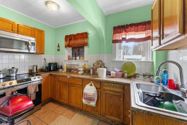 kitchen with sink, light tile patterned floors, ornamental molding, appliances with stainless steel finishes, and decorative backsplash