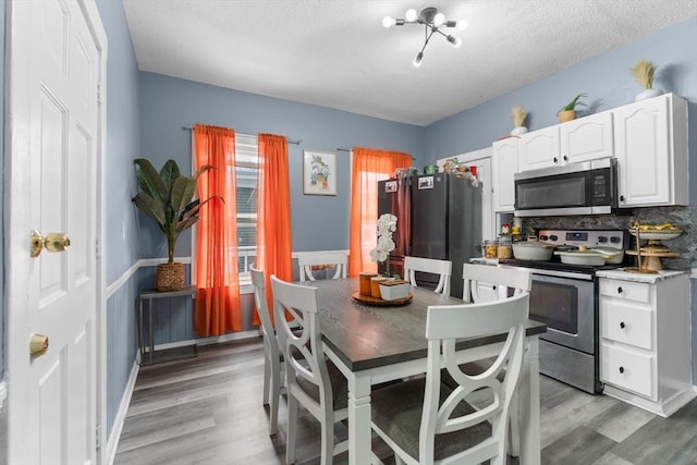 kitchen featuring white cabinetry, light hardwood / wood-style flooring, a textured ceiling, stainless steel appliances, and backsplash