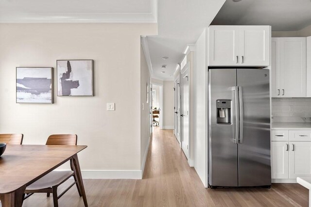 kitchen featuring white cabinetry, stainless steel refrigerator with ice dispenser, light wood-type flooring, decorative backsplash, and ornamental molding