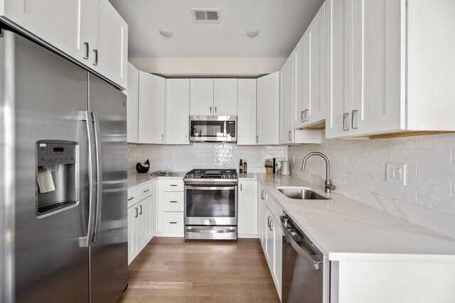 kitchen featuring white cabinets, appliances with stainless steel finishes, light stone countertops, and sink