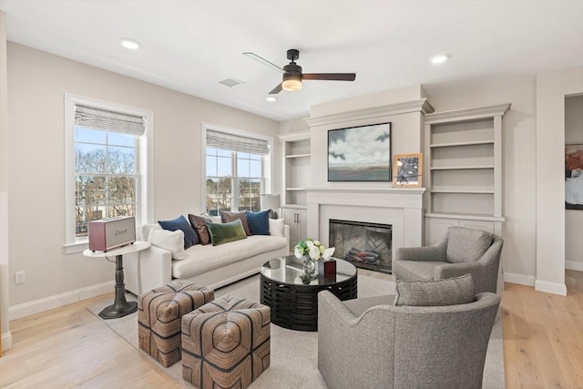 living area with recessed lighting, light wood-type flooring, baseboards, and a glass covered fireplace