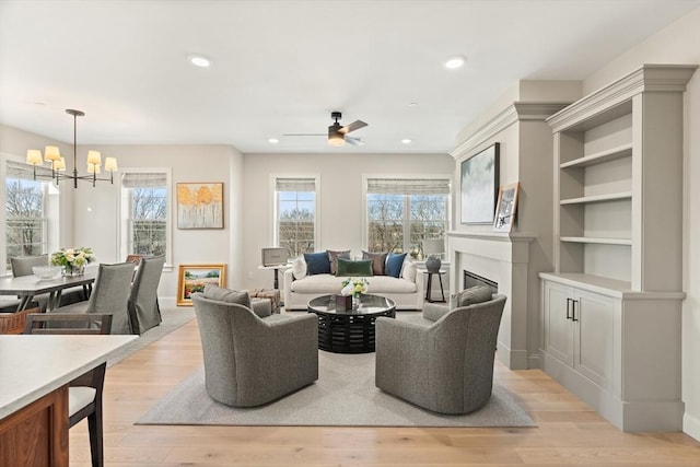 living area with a glass covered fireplace, recessed lighting, ceiling fan with notable chandelier, and light wood-type flooring