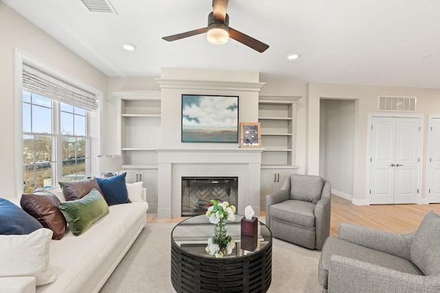 living room with light wood finished floors, visible vents, recessed lighting, and a glass covered fireplace