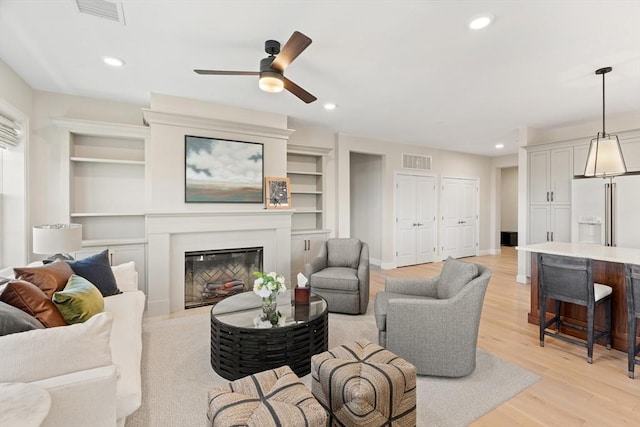 living room with recessed lighting, visible vents, light wood-style floors, and a glass covered fireplace