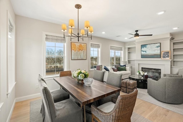 dining room featuring light wood finished floors, built in shelves, baseboards, recessed lighting, and a glass covered fireplace