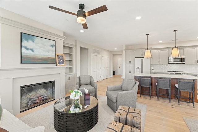 living area featuring a glass covered fireplace, recessed lighting, visible vents, and light wood finished floors