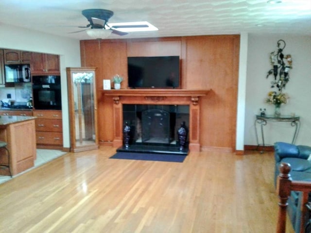living room with a ceiling fan, a tile fireplace, light wood-style floors, and baseboards
