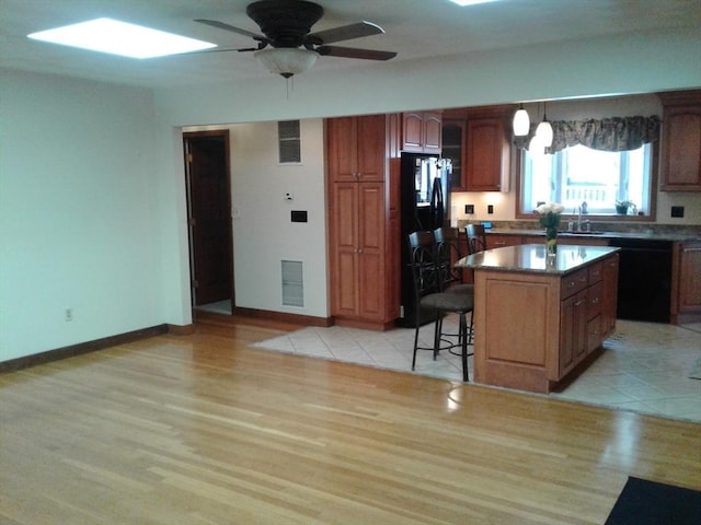 kitchen featuring black appliances, a sink, light wood finished floors, and a breakfast bar area