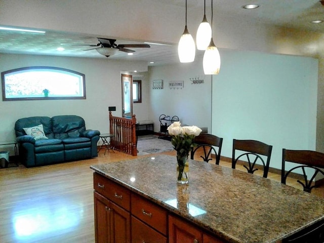 kitchen featuring a ceiling fan, dark stone counters, decorative light fixtures, light wood-type flooring, and recessed lighting
