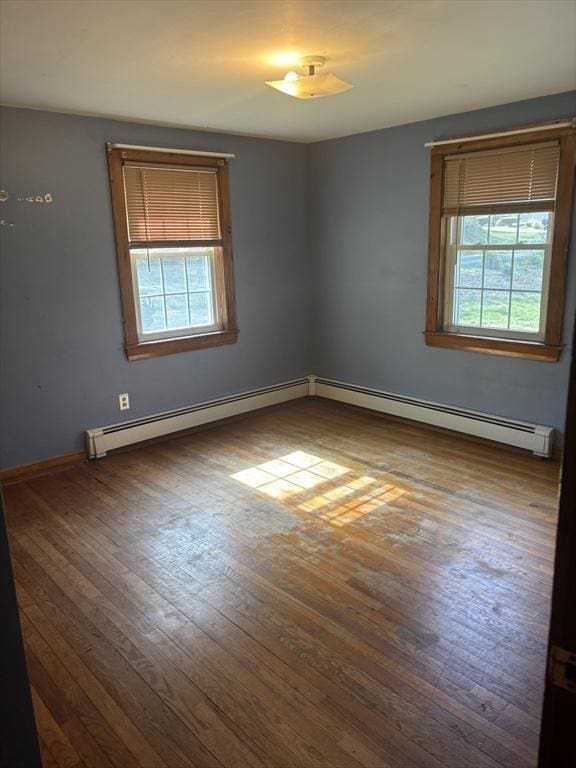 empty room with baseboards, a baseboard heating unit, and wood finished floors