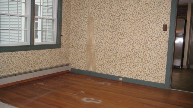 unfurnished room with baseboards, wallpapered walls, wood finished floors, and a baseboard radiator
