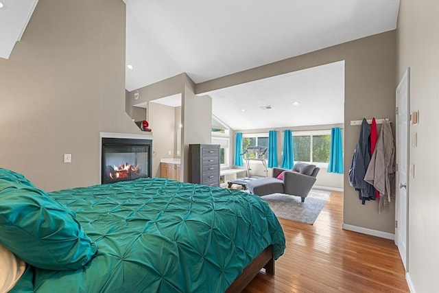 bedroom featuring baseboards, a glass covered fireplace, lofted ceiling, and hardwood / wood-style floors