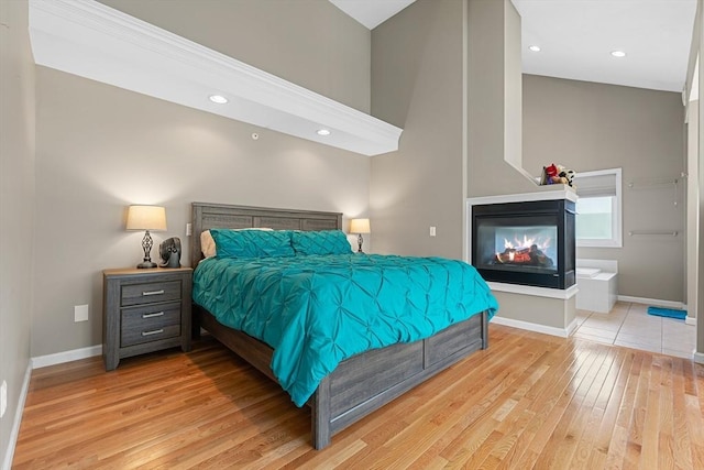 bedroom with baseboards, recessed lighting, a multi sided fireplace, and wood finished floors
