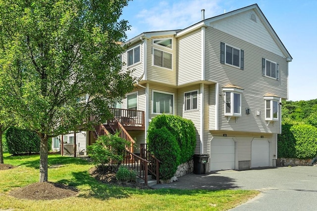 view of front of property featuring aphalt driveway, a garage, a wooden deck, stairway, and a front yard