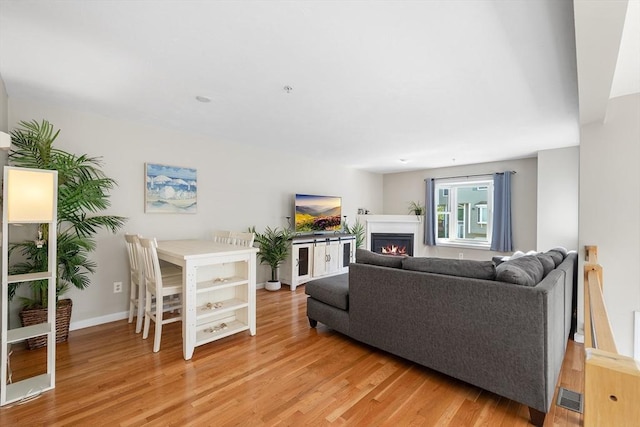living area featuring baseboards, visible vents, light wood-type flooring, and a warm lit fireplace